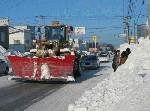 街は除雪車が行きかっている。雪の壁をくりぬいたバス停(右側)には、車道を歩かないといけない。バスに乗るのも命がけ?!